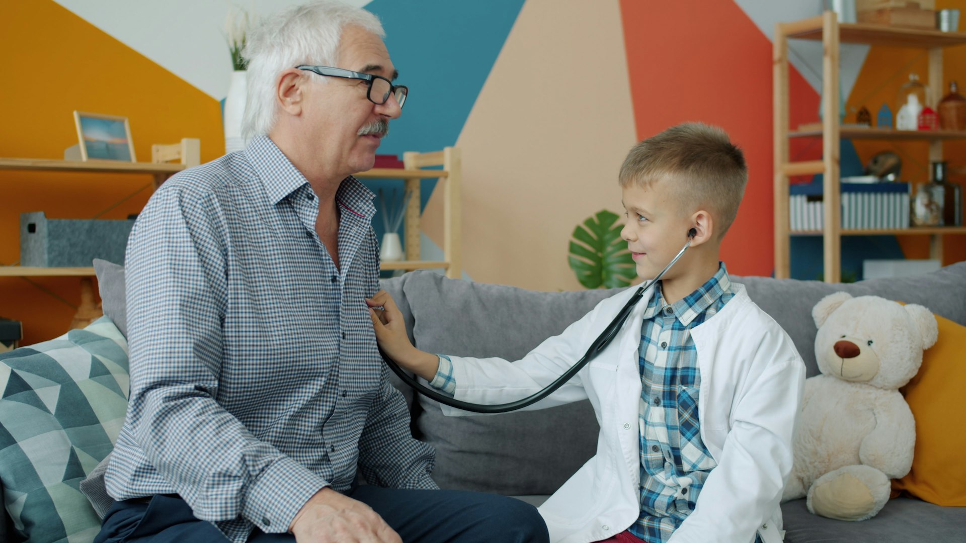 Boy in doctor's coat listens to grandfather's chest